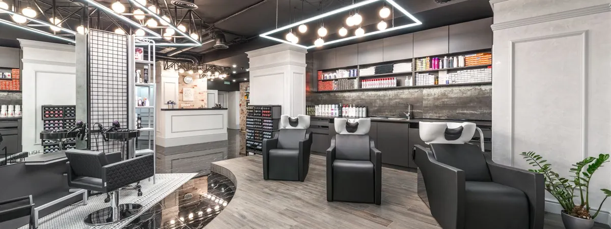 A hair salon with the chairs in a row, the backwash basins at the far end and products on the shelves along the wall.